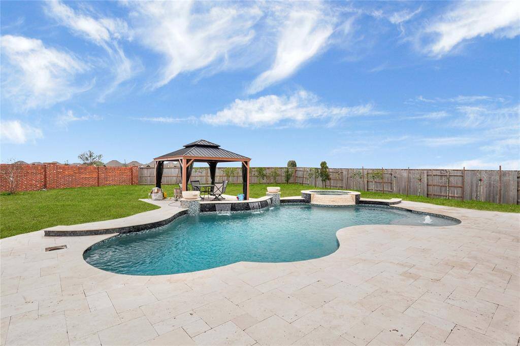 The expansive, oasis-style backyard boasts a luxury custom-built pool with a hot tub, all elegantly surrounded by a travertine patio. A charming gazebo offers the perfect retreat for relaxation and outdoor enjoyment.