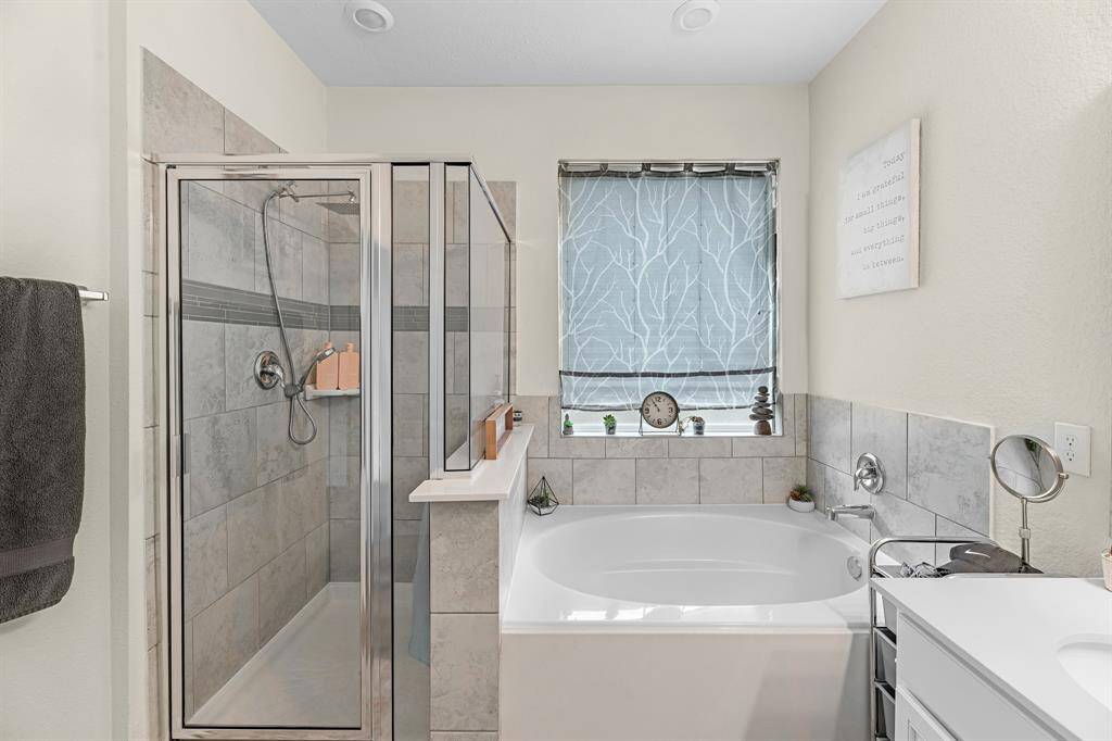 The bathroom wouldn't be complete without a glass-enclosed shower and a large soaking tub.  The window allows natural light, enhanced by a decorative shade.