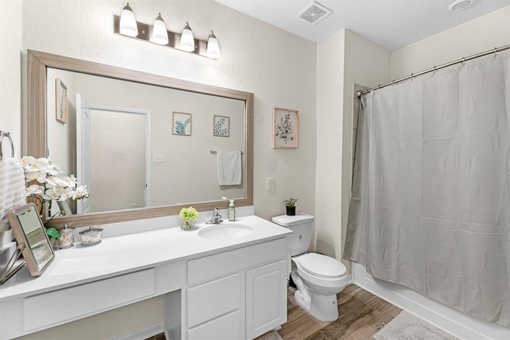 This secondary bathroom features a clean, modern design with a large mirror above the large vanity. It includes a tub/shower combo.