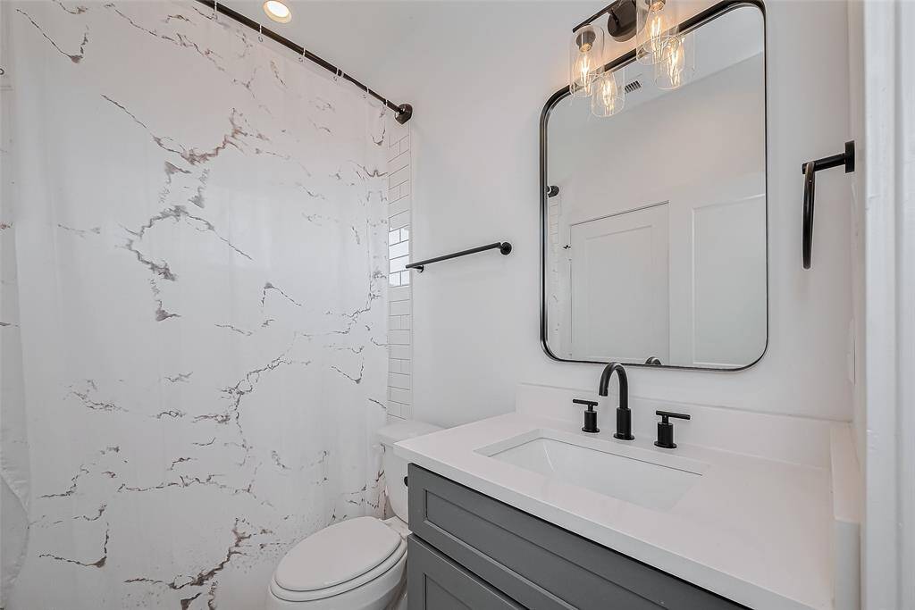 This beautifully updated bathroom features a sleek vanity with matte black fixtures, a framed mirror with modern lighting, and a tiled shower-tub combo—delivering both style and comfort in one elegant space.