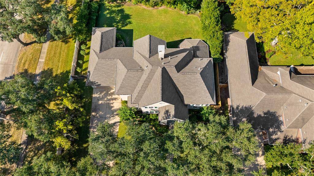 An aerial view of the house showcasing its two-story stucco exterior, oversized backyard, and surrounding area, including the lush greenery, adds to the charm of the property.