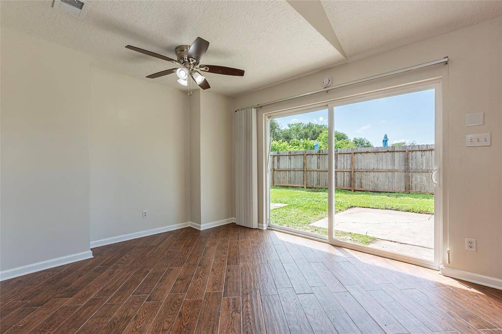 Spacious living room with vinyl plank flooring, high ceilings, ceiling fan fixtures and backyard views through large windows.