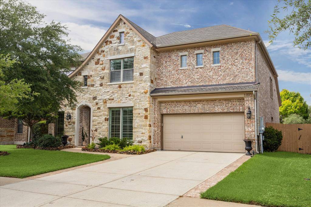 This elegant two-story home features a stone exterior, a two-car garage, and a thriving front yard. An arched entryway and large windows add charm and curb appeal.
