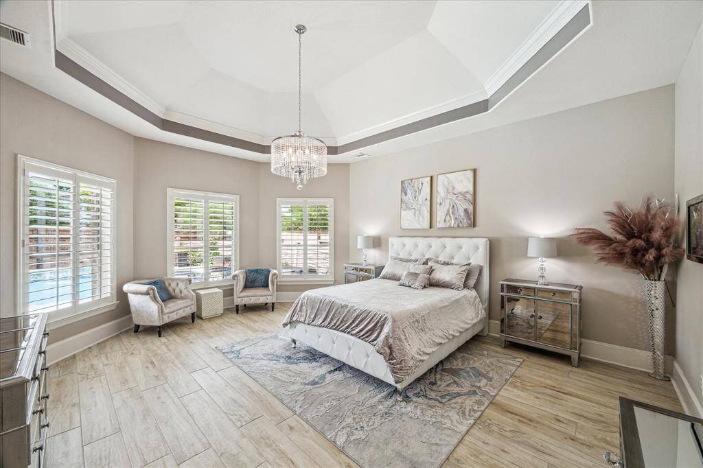 The spacious and elegant primary bedroom features a tray ceiling, a stylish chandelier, and beautiful views of the backyard oasis.