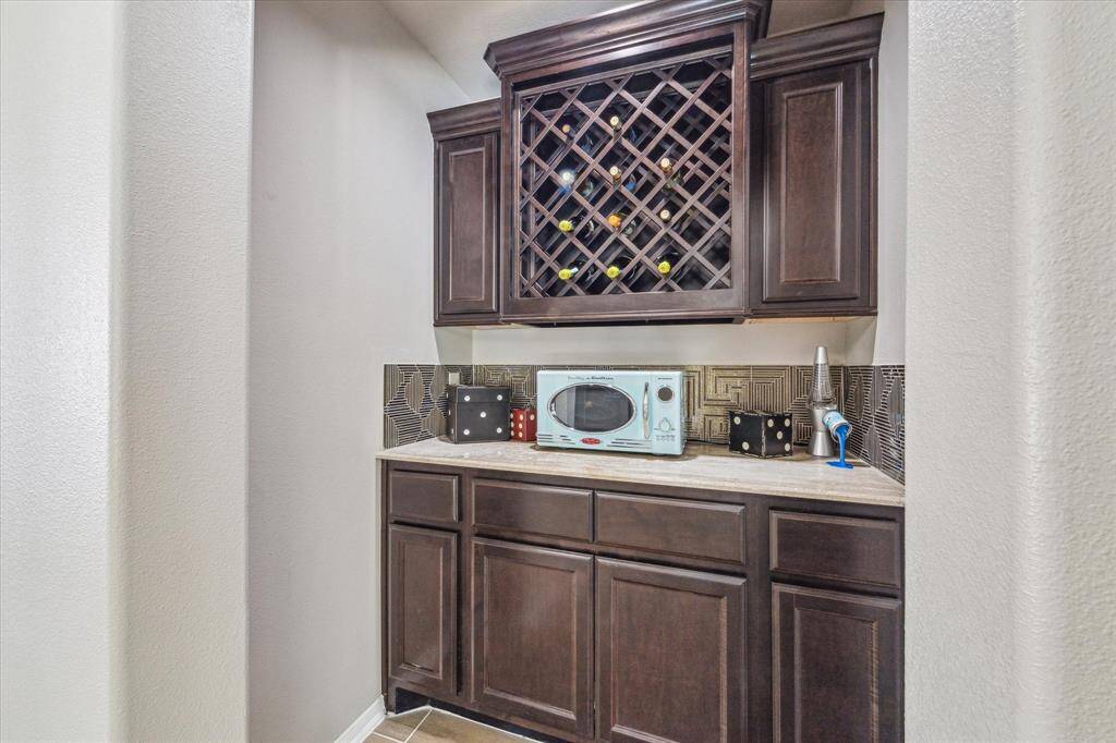 This stylish built-in wet bar ready features rich dark cabinetry, a wine rack, and a sleek tile backsplash. With ample storage space, it's perfect for entertaining or creating a convenient beverage station in the upstairs gameroom.
