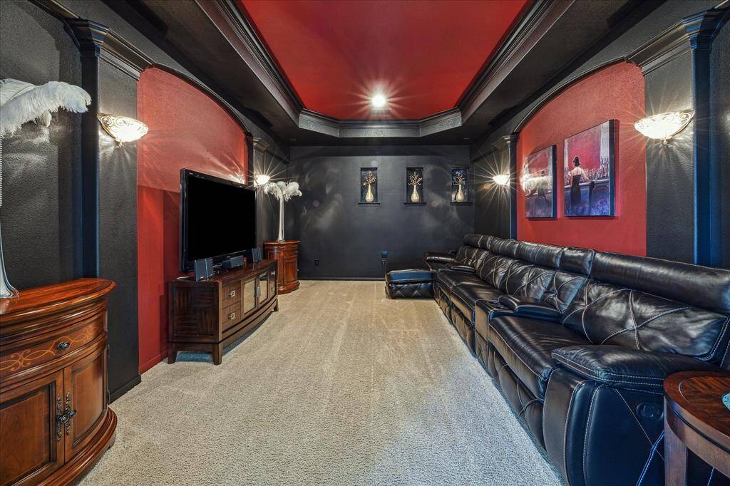 This impressive media room features bold red and black walls, detailed tray ceilings, and elegant wall sconces for ambient lighting.