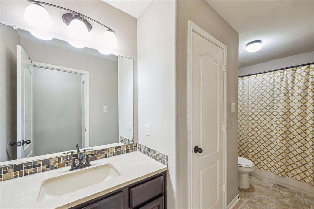 This upstairs secondary bathroom features a sleek tiled backsplash, a large mirror, and stylish lighting. Conveniently located off the game room and a secondary bedroom, it offers both function and modern design.
