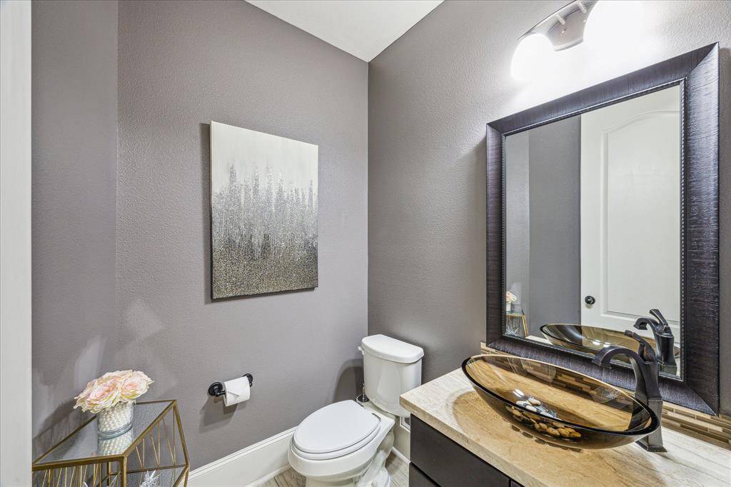 This elegant half-bath features modern finishes, including a sleek vessel sink with a stylish waterfall faucet, a framed mirror, and chic lighting. The neutral tones and artistic backsplash create a refined, contemporary look—perfect for guests.