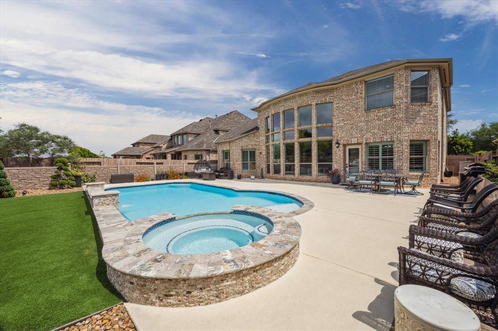 This close-up view highlights the inviting hot tub with stone surround, seamlessly integrated into the saltwater pool design. Set against the backdrop of the home's striking brick exterior and expansive windows.