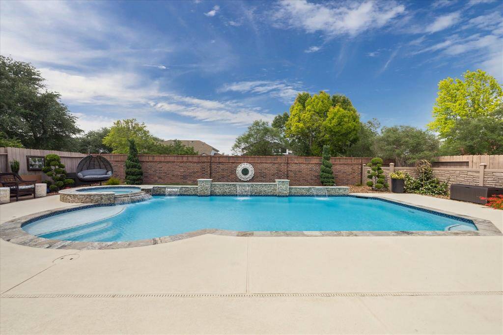 This view captures the serene beauty of the saltwater pool, complete with a built-in hot tub and tranquil waterfall features. Surrounded by manicured landscaping and a full brick privacy wall, the backyard offers a peaceful, resort-style escape with no back neighbors.