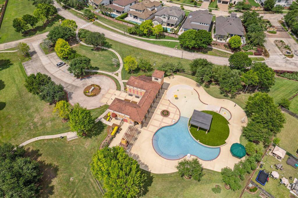 This aerial view showcases the vibrant community pool and recreation area, complete with a large resort-style pool, shaded pavilion, splash pad, playground, and open green spaces. It's the perfect place for residents to relax, play, and connect with neighbors.