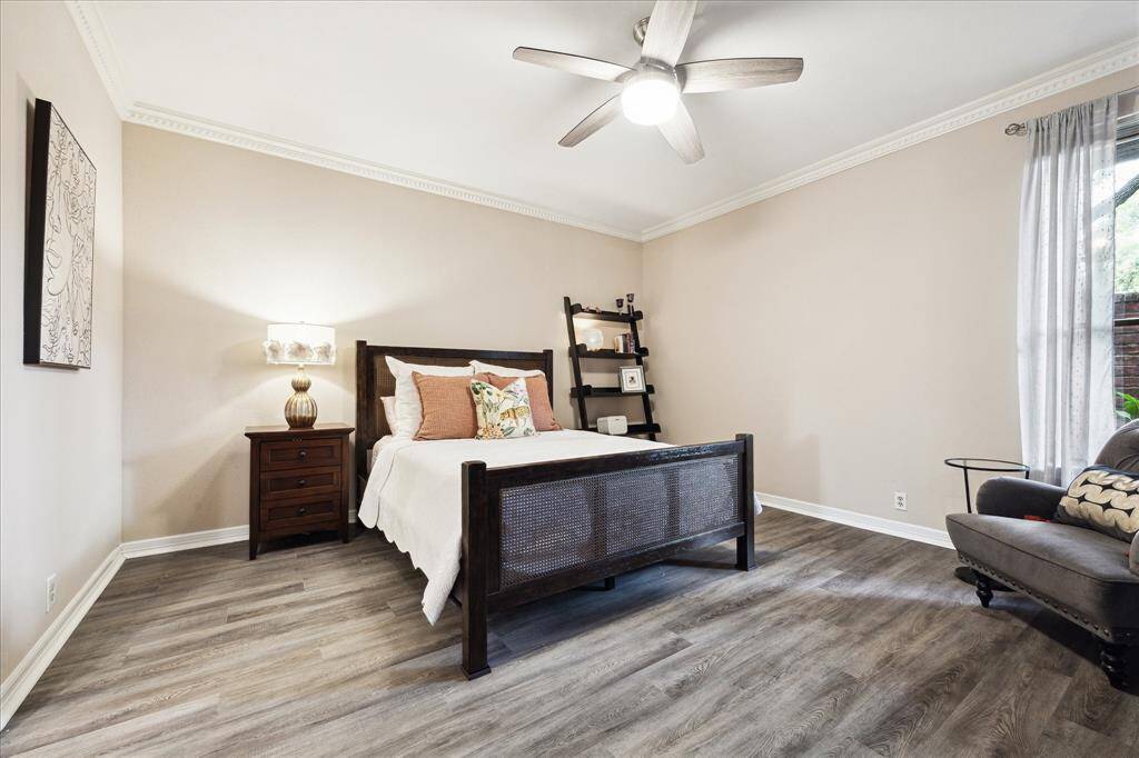 Large primary bedroom with crown molding, ceiling fan, light filled window overlooking the private patio, en-suite bathroom and a large walk-in closet with built-in storage shelves.