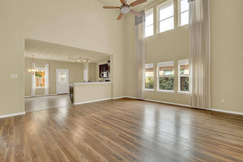 Warm wood flooring grounds this expansive living area, where elevated ceilings and oversized windows contribute to a bright, airy feel. The open layout enhances flow and function, making it ideal for both everyday living and entertaining.