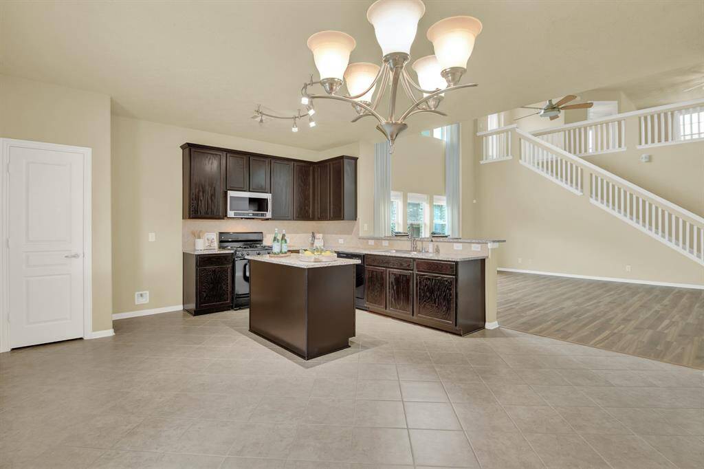 The rich, dark cabinetry offers generous storage and a refined contrast against the lighter elements of the room. The open layout flows into the dining area, where a contemporary chandelier adds a touch of sophistication