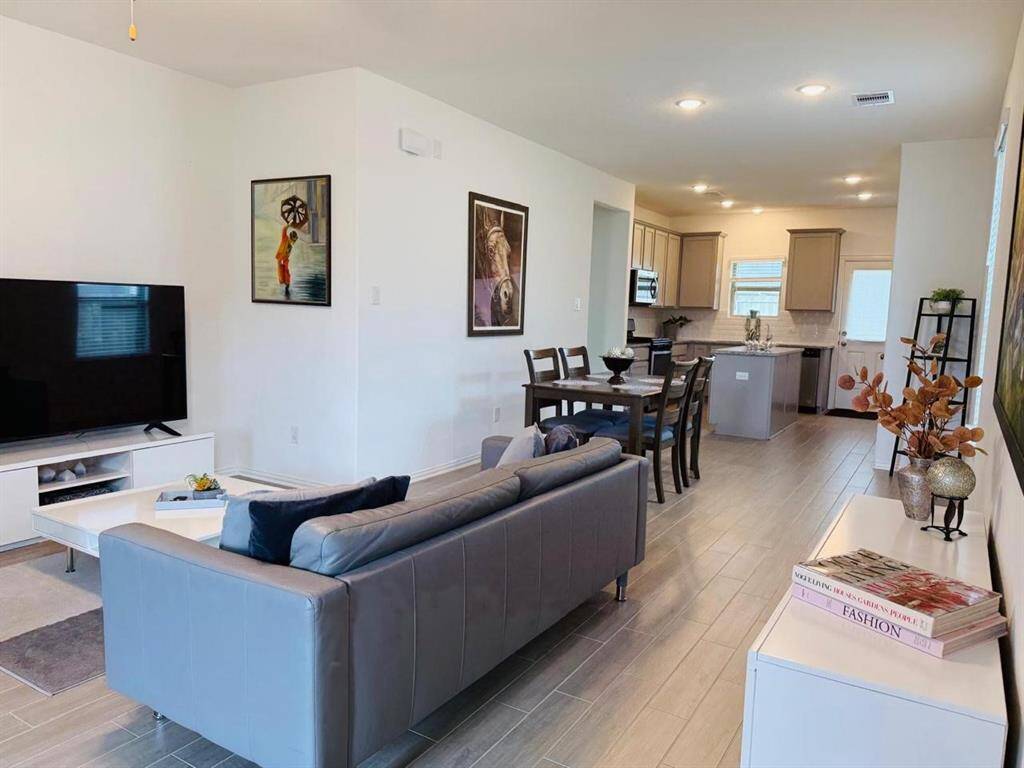 The living room offers a modern yet cozy atmosphere, featuring sleek tile floors and an open layout that flows seamlessly into the kitchen and dining area.