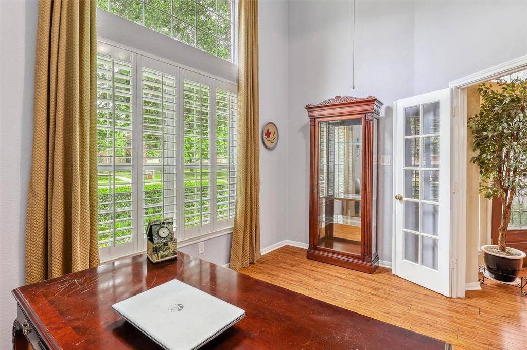 The study features a soaring ceiling, gleaming hardwood floors, & large windows with classic plantation shutters. Abundant natural light fills the room, creating a bright, inspiring environment ideal for productivity and focus.