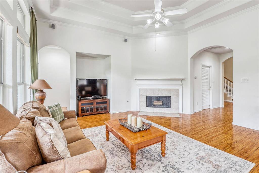 At the heart of the room, a romantic fireplace with a beautifully tiled surround and classic wooden mantle creates a cozy focal point—perfect for quiet evenings or entertaining guests. An adjacent entertainment nook provides a stylish and functional space to house your media center, blending practicality with refined design.