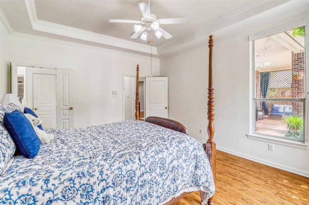 A high tray ceiling with a ceiling fan adds architectural depth, while gleaming hardwood floors and elegant crown molding enhance the room’s timeless charm. The luxurious en-suite bathroom completes the experience, offering a spa-like setting.