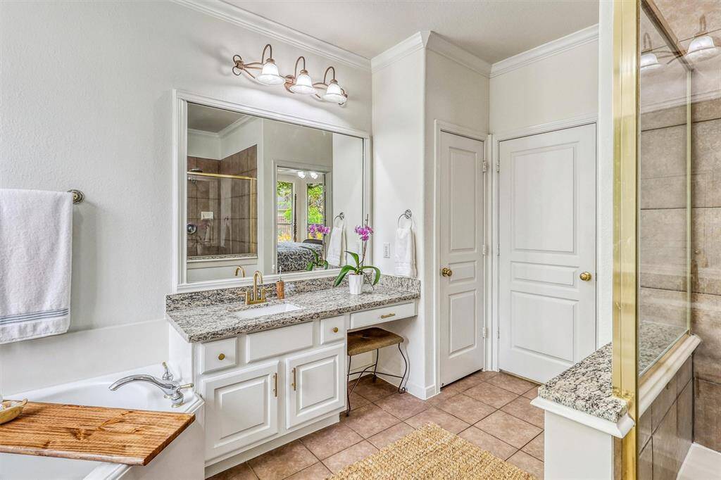 Dual his-and-her vanities are topped with rich granite countertops, each accented by framed mirrors and stylish vanity lighting for a polished look.