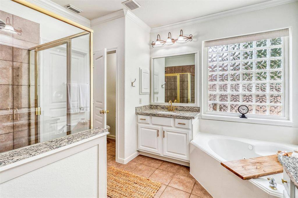 A soothing corner jetted tub rests beneath a glass block window, offering both privacy and natural light.