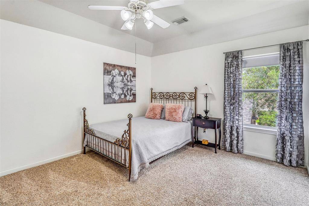 This generously sized secondary bedroom offers comfort and style, featuring a high ceiling with a ceiling fan, soft plush carpeting, and a large window that fills the space with natural light. A walk-in closet provides ample storage, making this room both functional and inviting—perfect for family, guests, or a personalized retreat.