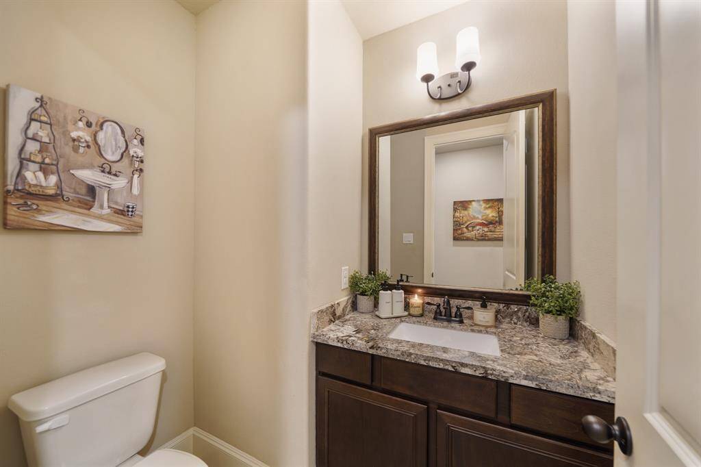 This half bathroom features a sleek vanity with a granite countertop, elegant mirror, and modern lighting.