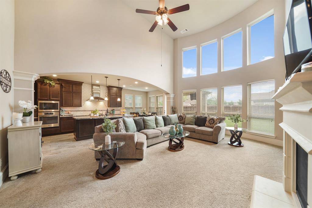 This spacious, open-concept living area features high ceilings, large windows for natural light. It seamlessly connects to a modern kitchen with dark wood cabinets and stainless steel appliances, creating an inviting space for family gatherings and entertaining.