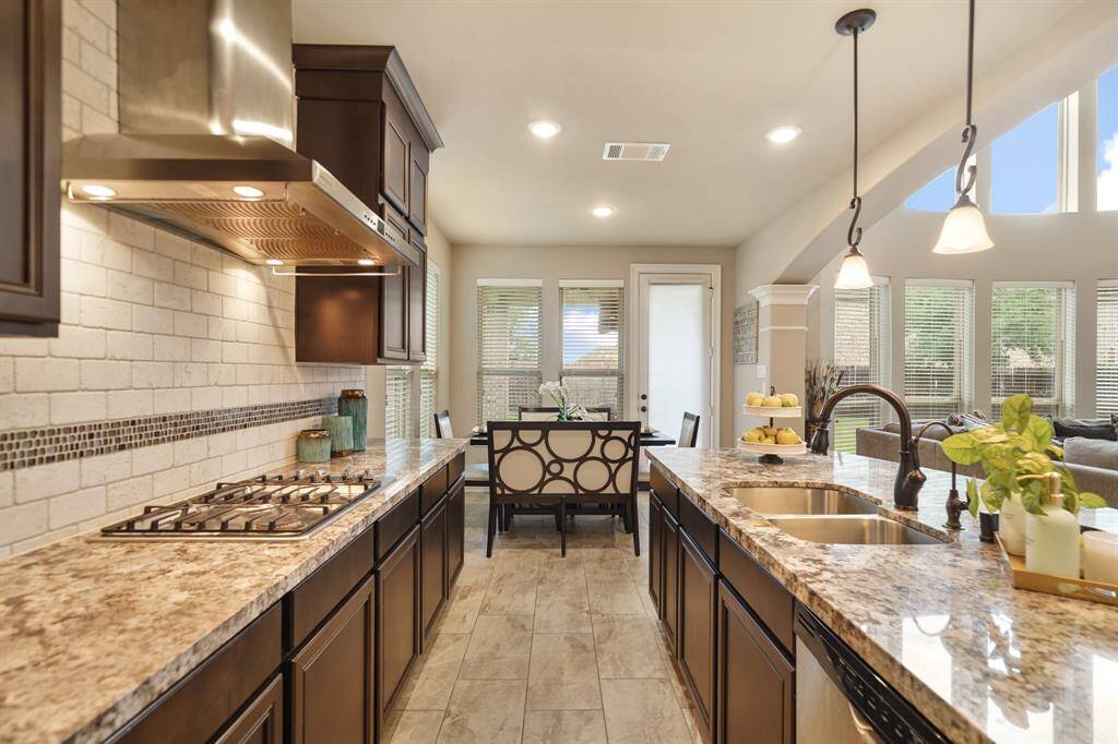 This kitchen boasts modern elegance with granite countertops, a spacious island with a double sink, and sleek stainless steel appliances. Ample natural light fills the space through large windows, enhancing the open and airy feel. The adjacent breakfast nook and living space create a seamless flow, perfect for entertaining.