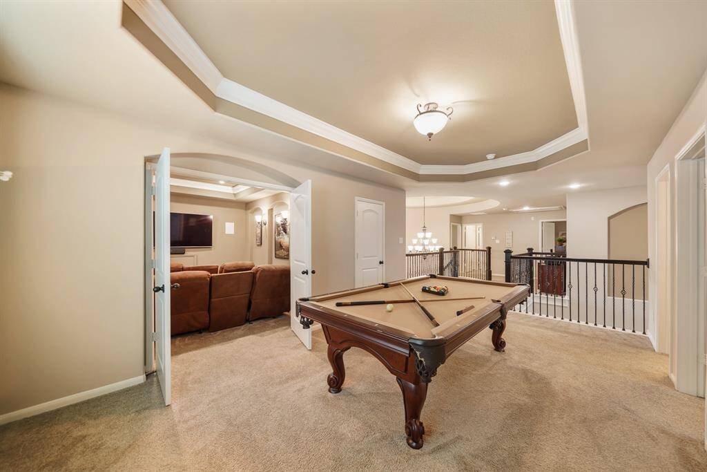 This spacious game room features a stylish pool table and leads into a cozy media room with comfortable seating. The open layout is enhanced by elegant lighting and a modern railing, creating a perfect entertainment space.