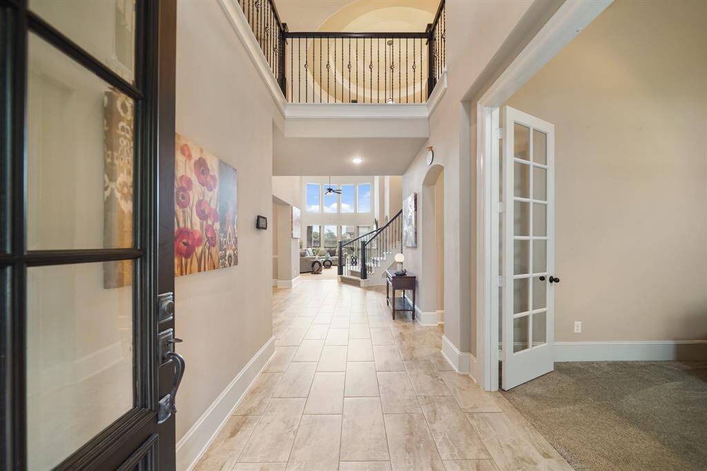 The photo showcases an inviting entryway with a high ceiling, elegant tile flooring, and a view into a spacious living area. The space is well-lit, featuring a staircase with wrought iron railings and tasteful decor.