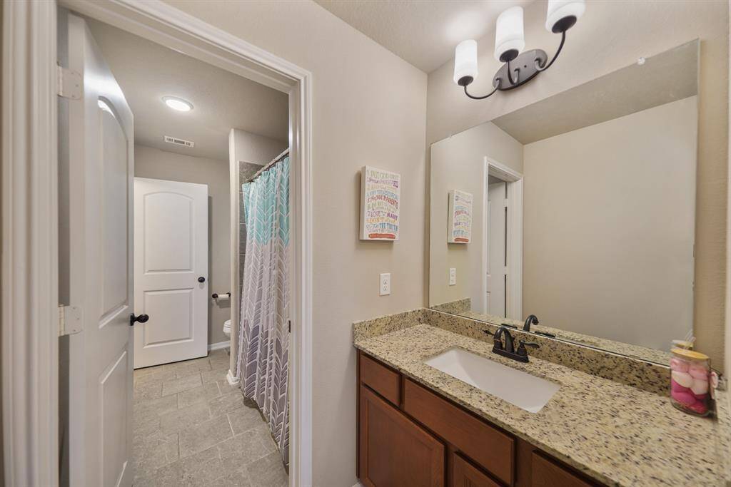 This jack-and-jill bathroom features a granite countertop with a sink, a large mirror, and modern lighting fixtures. It includes a shower area, neutral tile flooring, creating a clean and inviting space.