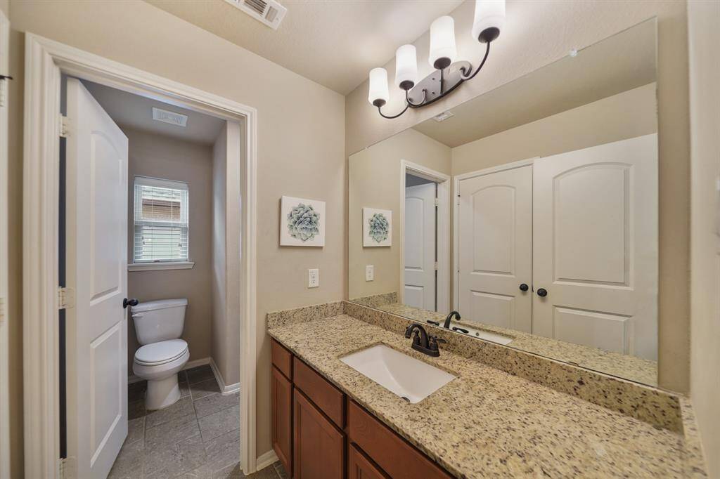 This photo showcases a modern bathroom featuring a granite countertop with a single sink, elegant lighting, and a separate toilet area with a window for natural light.