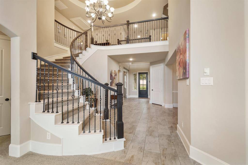 This photo showcases a spacious, elegant foyer featuring a grand curved staircase with wrought iron railings, high ceilings, and modern lighting fixtures.