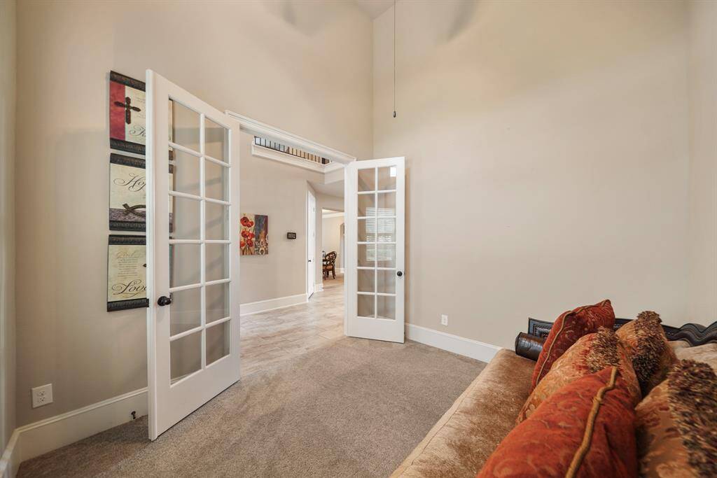 This photo shows a cozy flex space/in-home office with carpeted flooring and elegant French doors leading to a tiled hallway, creating an inviting and open feel.
