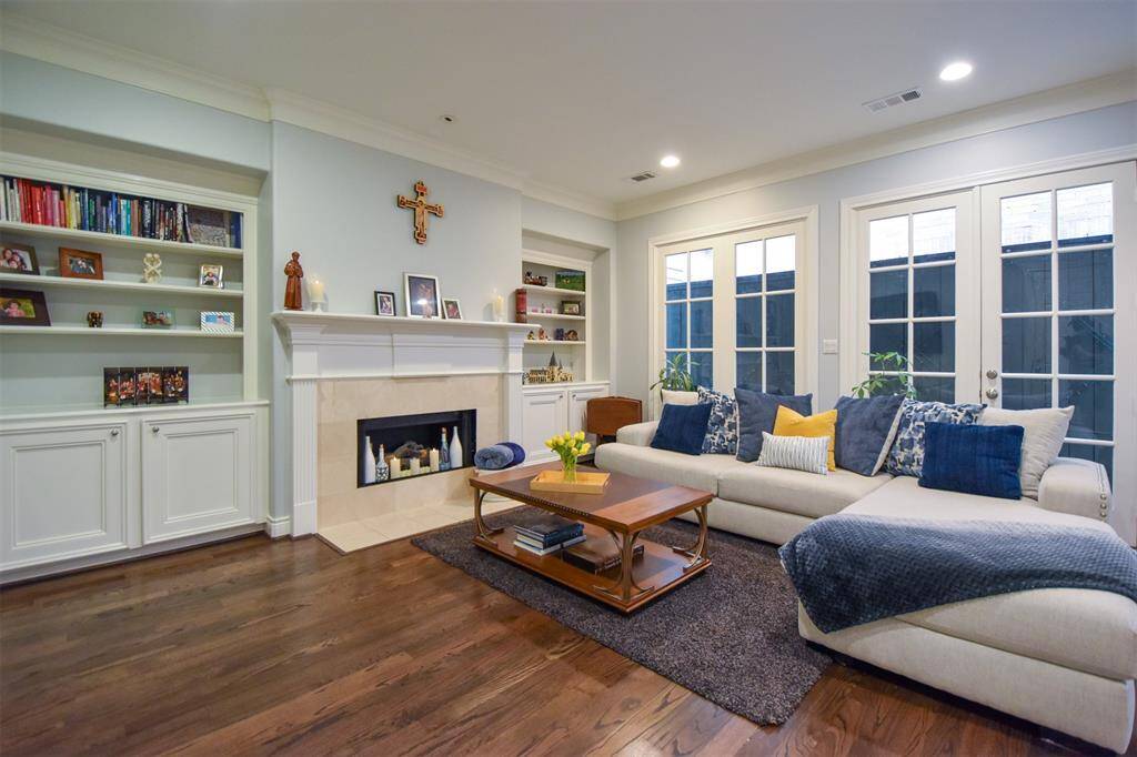 Cozy and elegantly appointed living space featuring built-in bookshelves, a classic fireplace, rich hardwood floors, and ample natural light from French doors