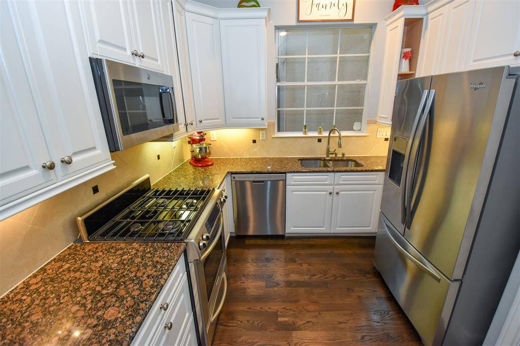 This is a modern kitchen featuring stainless steel appliances, white cabinetry, granite countertops, and hardwood flooring