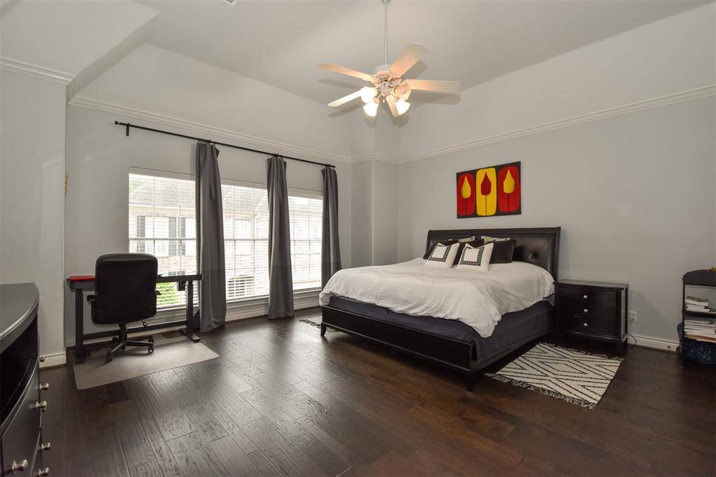 Spacious primary bedroom with hardwood floors, large windows with custom drapes and high ceiling. It has ample space for a work desk and additional furniture