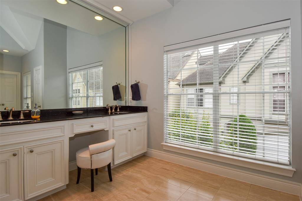 Primary bathroom featuring a large vanity with dual sinks, granite counters, ample cabinetry, and a built-in dressing table. There's a large window with blinds offering natural light