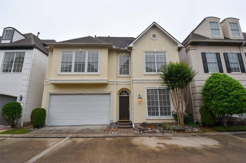 This is a 3 story townhouse featuring a two-car garage, arched entryway, and symmetrical second-story windows. Landscaping includes mature shrubs and a small tree. It's part of a row of homes with similar architectural styles