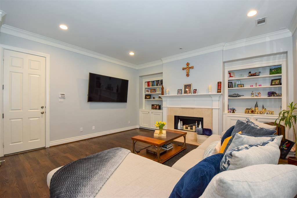 Generous sized, well-lit family room featuring hardwood floors, a fireplace with a white mantel, built-in shelving. The room is finished with crown molding and has a neutral color scheme, offering a comfortable and inviting space