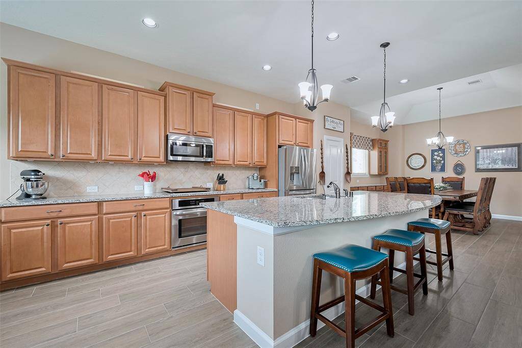 This spacious kitchen includes a large island with seating for three, modern pendant lighting, and an open layout that connects to a dining area, perfect for entertaining.