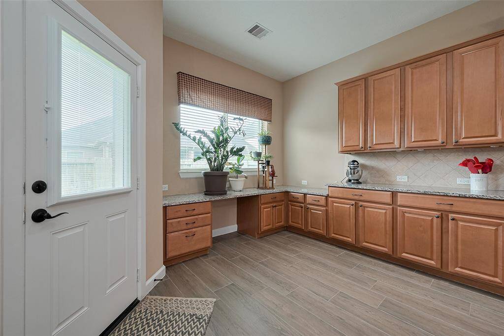 This photo shows a bright, spacious kitchen area with ample natural light. It features light wood cabinetry, a tiled backsplash, and a countertop with plenty of workspace.