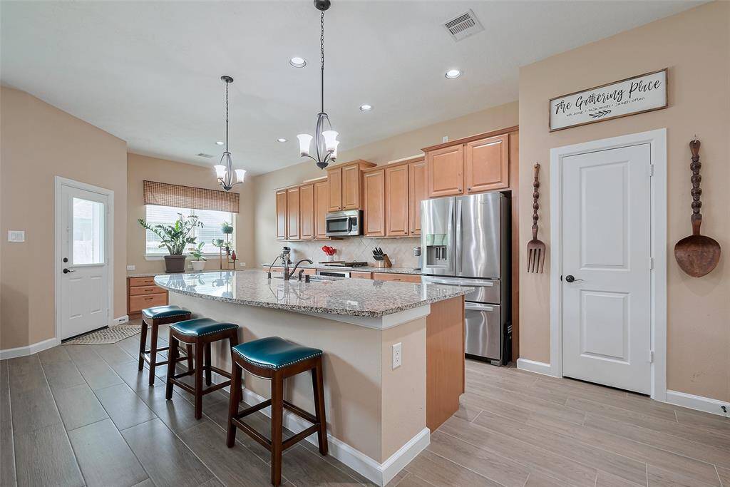 This kitchen features modern amenities with stainless steel appliances, a large granite island with bar seating, and ample wooden cabinetry. The space is bright and inviting, offering a cozy dining area by a window.