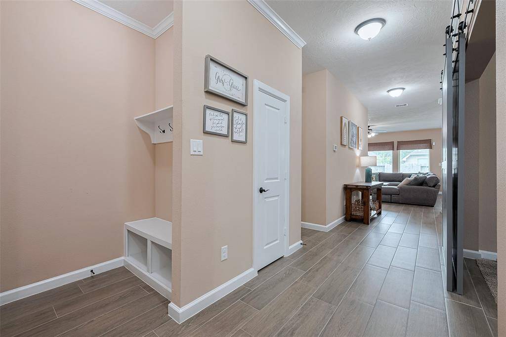 This photo showcases a modern, inviting entryway with warm-toned walls and wood-look tile flooring. It features a small bench with hooks for storage, leading into a cozy living area with large windows.