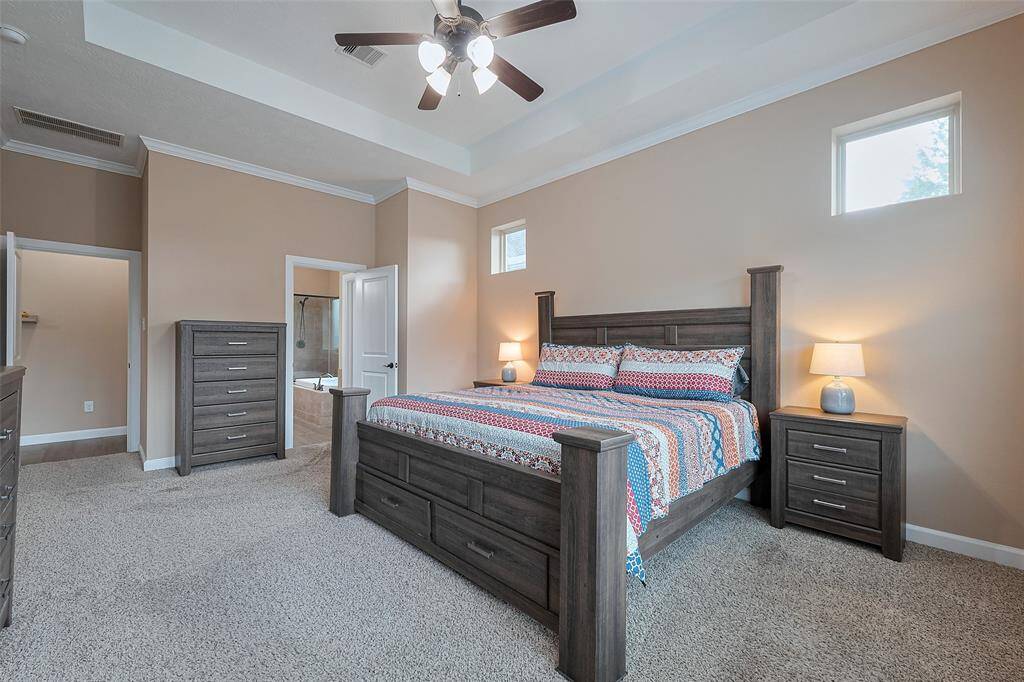 Natural light enters through two small windows, and an adjoining bathroom is visible through an open door of the primary bedroom with ensuite bath.