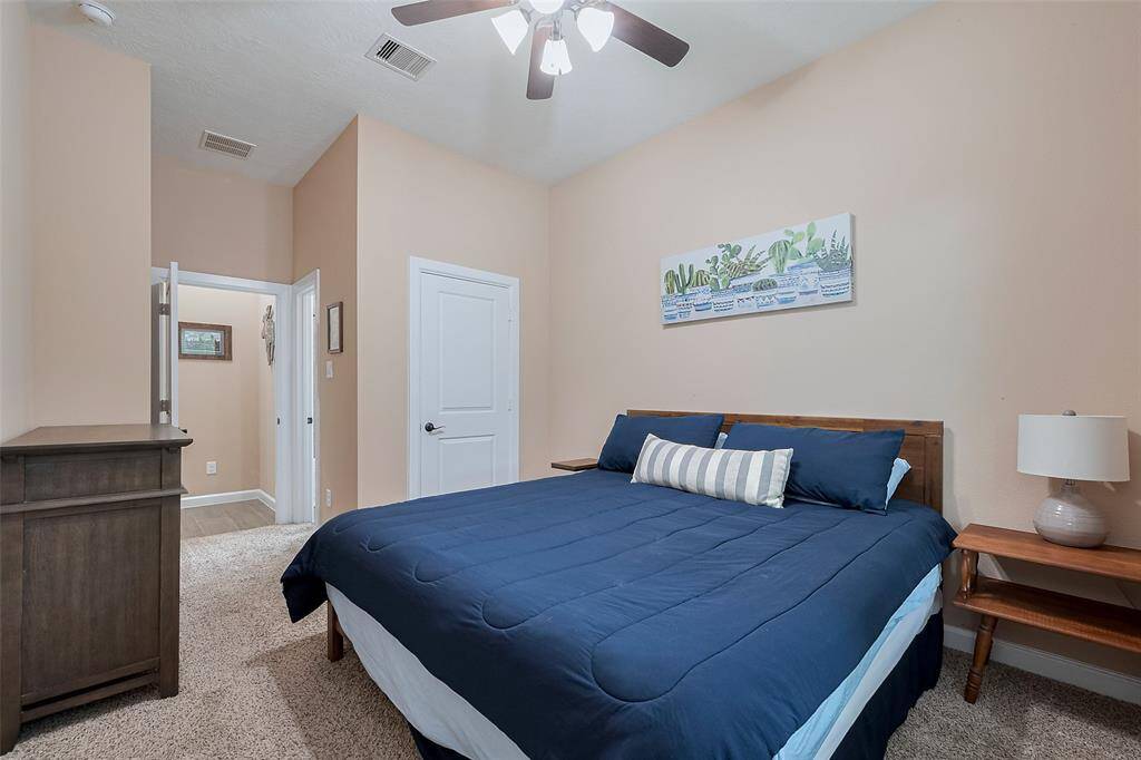 This cozy bedroom features neutral walls, a ceiling fan, and a plush carpet.