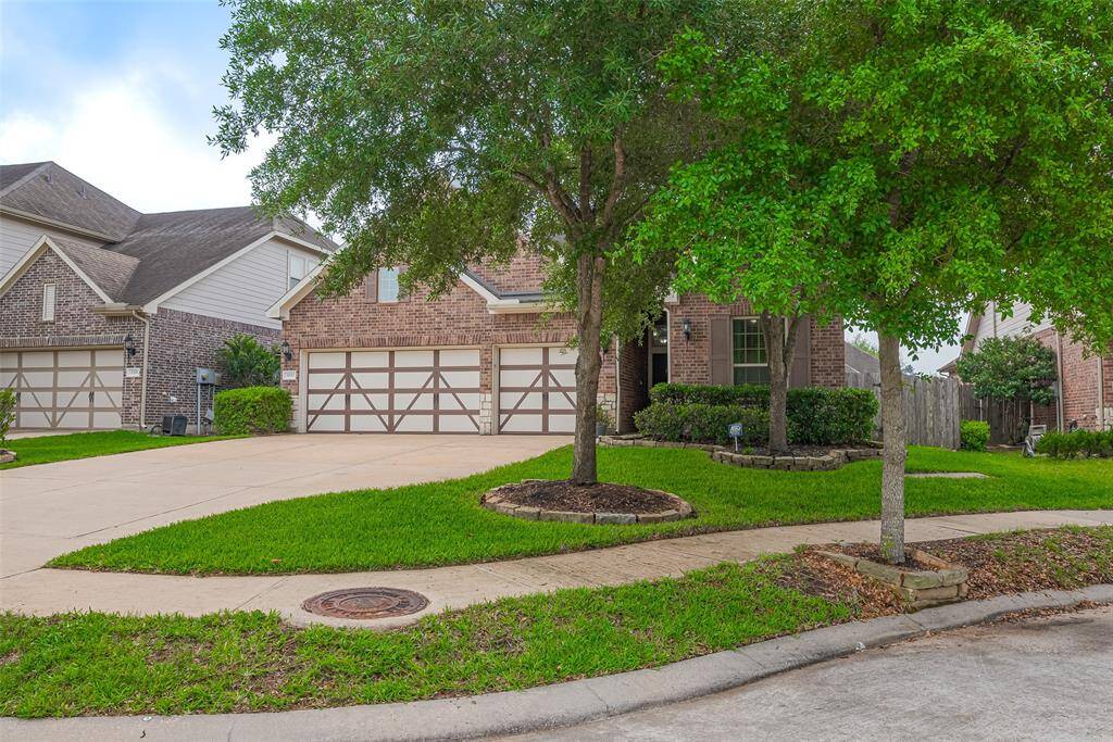 This photo showcases the charming brick home with a three-car garage and a well-maintained front yard. The driveway is spacious, and mature trees provide shade and curb appeal.