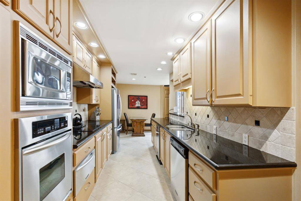 Galley-style kitchen featuring modern stainless steel appliances, ample cabinetry, and granite countertops. A serving hatch connects it to the adjacent room, enhancing the open feel.