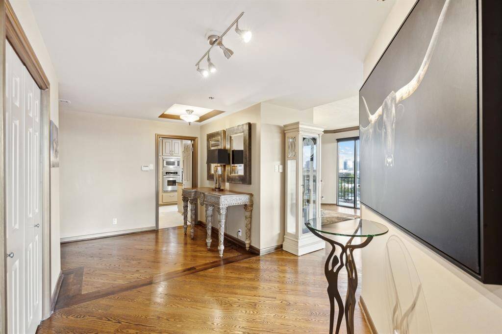 Upon entering, you see elegant hardwood floors, classic decorative trim, and large mirrors that enhance the sense of space. Natural light pours in from the adjacent balcony.