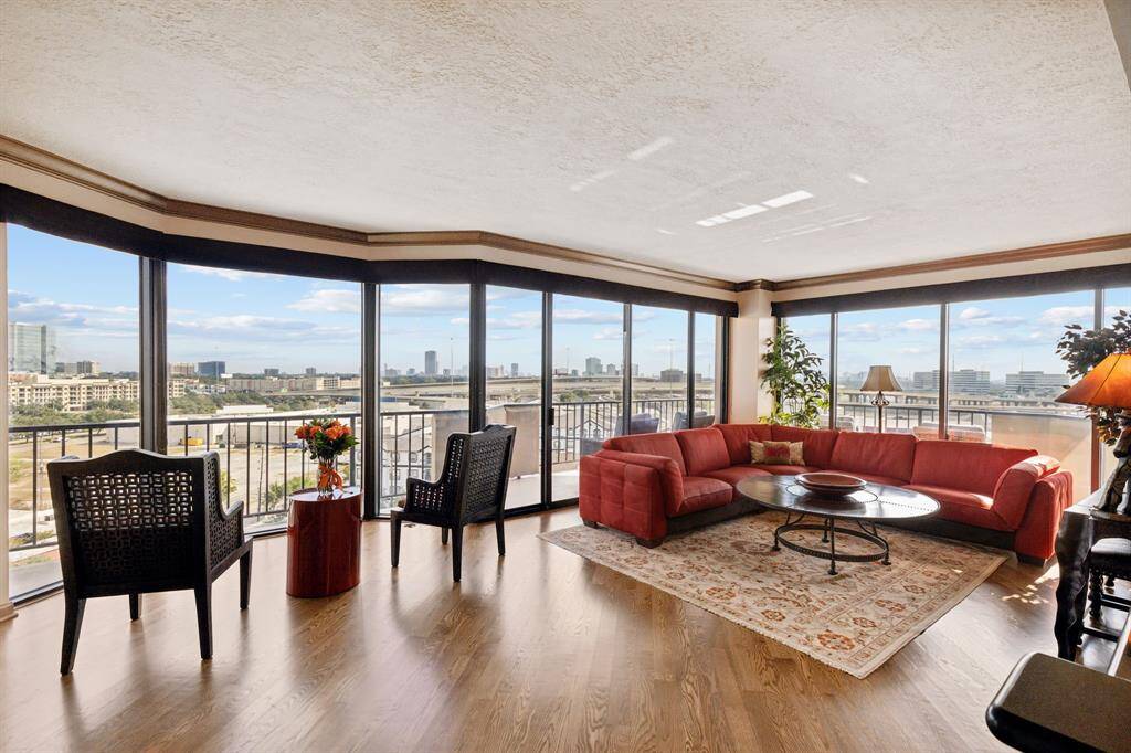 Spacious living room with large, panoramic windows offering impressive city views, sleek hardwood flooring, and a comfortable seating area.